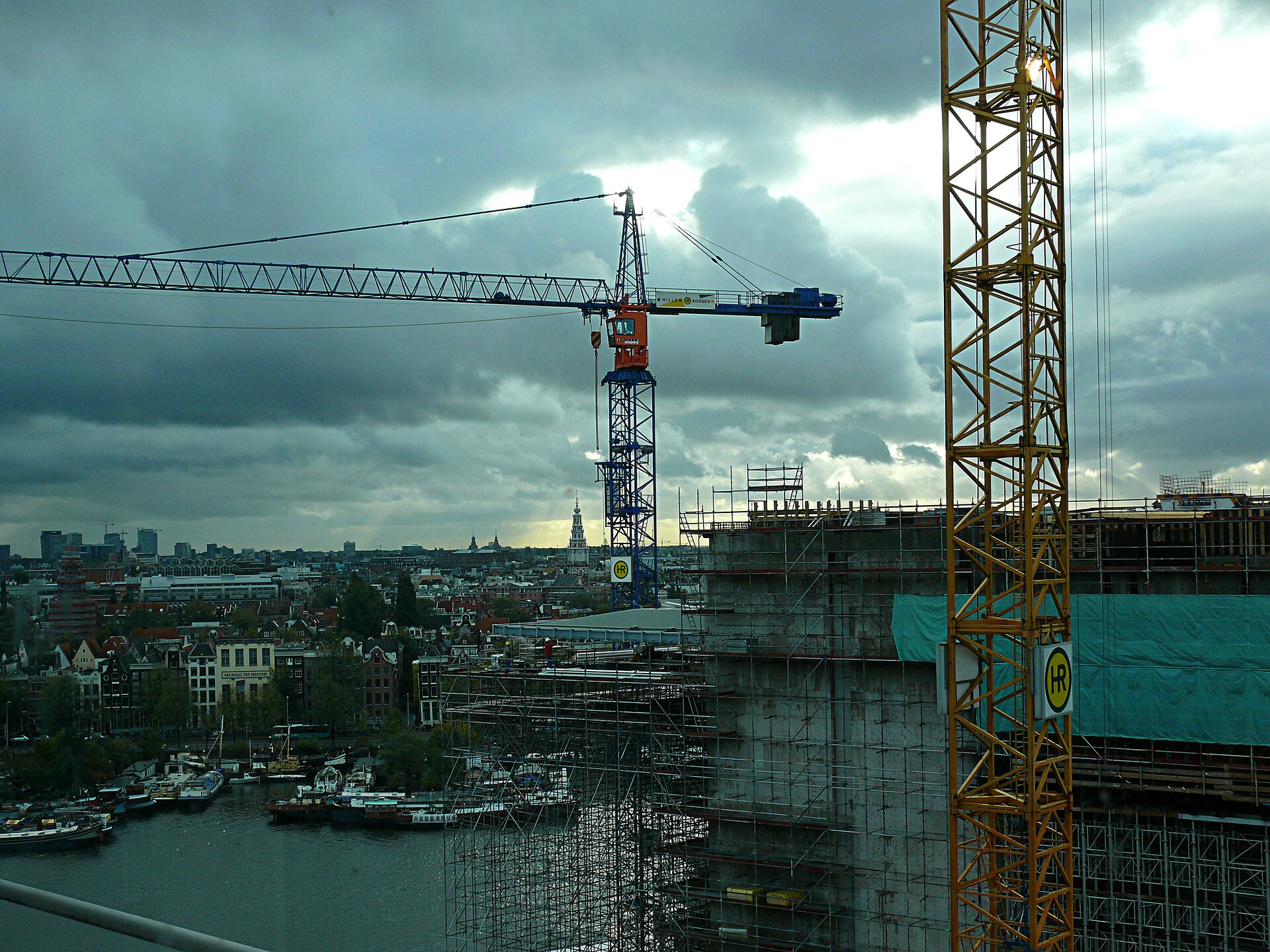 A construction site in late afternoon light, tower cranes above scaffolding